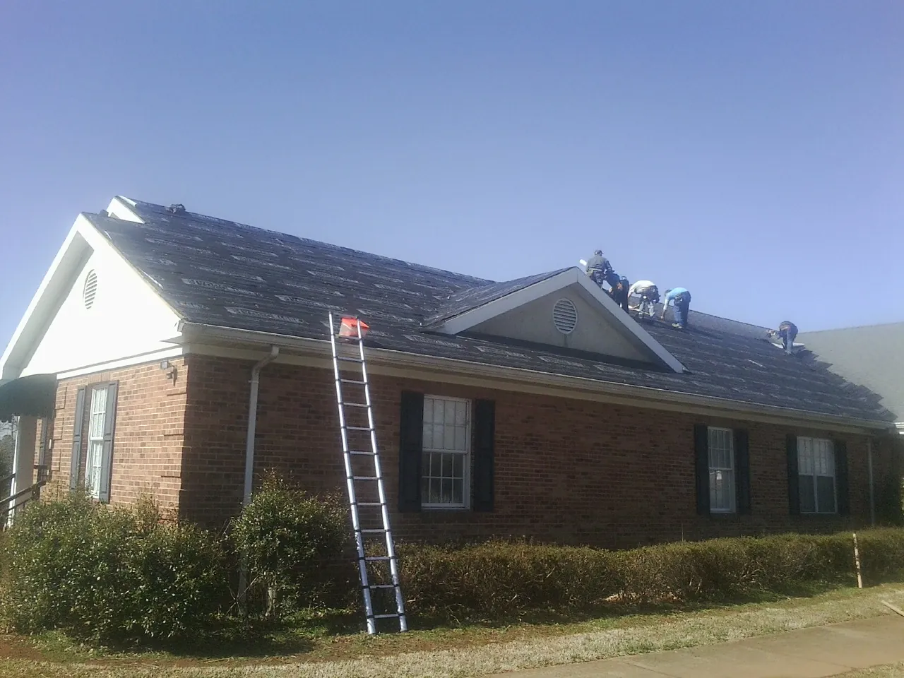 Crew tearing shingles off a brick ranch roof with a ladder set — Emergency Roof Repair work by our crew in Greenwood