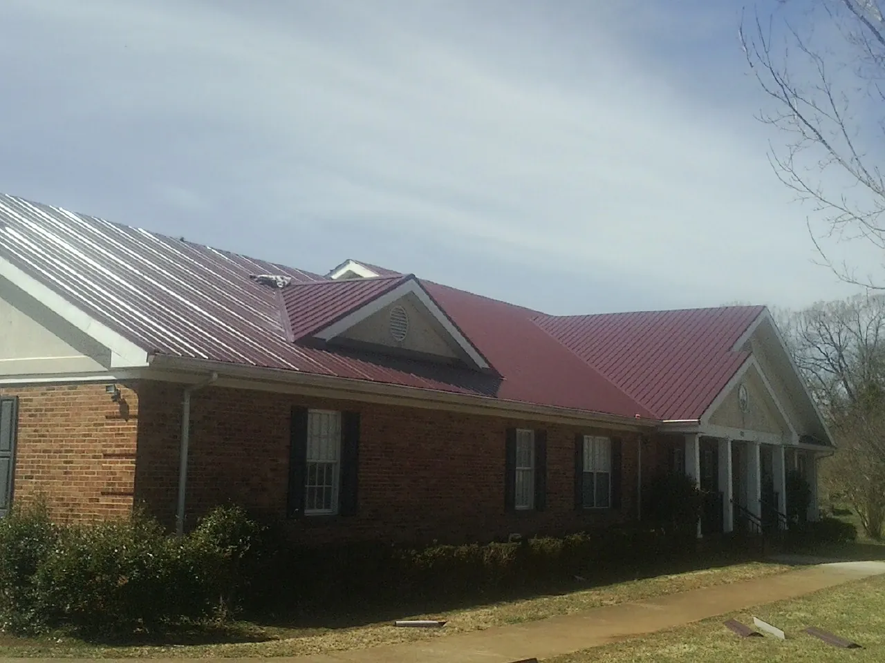 Red metal roof with gabled entries on a long brick building, from a Hail Damage Roof Repair job in Greenwood